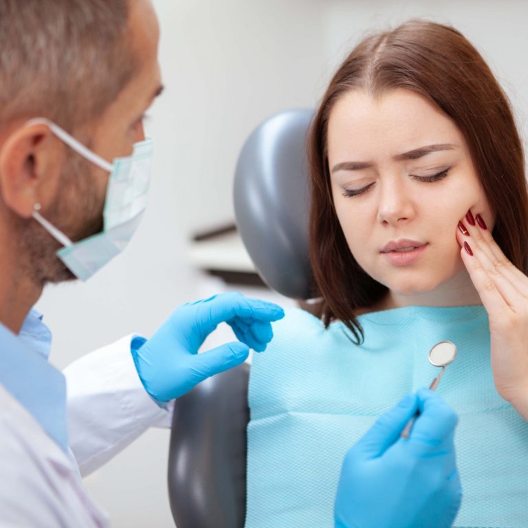 Young woman having toothache, sitting in a dental chair at the clinic. Female patient with terrible toothache visiting dentist